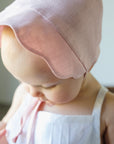 Close-up of baby wearing a shell pink linen scallop bonnet with a soft sun brim.