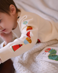 Close-up of a toddler's arm in a Hungry Caterpillar sweater, showing embroidered snacks like watermelon, cupcake, and lollipop