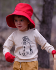 a child dressed in a cozy Paddington Bear sweater and red bucket hat