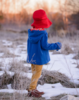 Back-facing view of a child in a cozy winter outfit, featuring a red hat and blue coat,