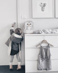 Toddler wearing the Flopsy Bunny Coat with floppy-eared hood, reaching for a door handle in a softly lit nursery.