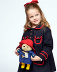 Young girl in a dark blue wool coat with gold buttons holds a Paddington Bear soft toy, featuring a red hat, blue wool coat, and yellow boots