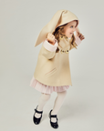 Young girl playing in Luxe Bunny Coat in Sand & Pink, featuring long bunny ears, wool fabric, and pink-lined cuffs.