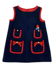 Navy blue girls' dress with decorative pockets and red trim, bow details, and a mini plush Paddington Bear in one of the pockets.
