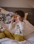 Child wearing the Kids Sweater in ivory, featuring a black knit illustration of Paddington Bear by Peggy Fortnum. Soft 100% cotton, gender-neutral