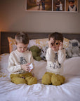 Two kids wearing ivory Paddington Bear sweaters, sitting on a bed