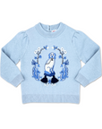 Light blue sweater with puffed shoulders, rib-knit details, and an intarsia-knit dog-and-dragon motif on a tasseled cushion