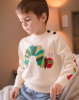 A cozy beige knit Hungry Caterpillar sweater worn by a child, featuring a vibrant caterpillar and embroidered food illustrations.