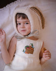 Ivory linen romper with embroidered bunny in a basket, adjustable straps, and button closures. Gender-neutral baby and toddler outfit