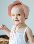 Baby wearing a pink linen scallop bonnet with a sun brim, fully lined for comfort.