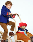 Child wearing a blue wool duffle coat A plush Paddington Bear in a red hat and blue coat rides in the wooden cart