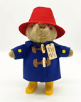 Paddington Bear plush in a blue duffle coat, red hat, yellow boots, and his iconic “Please look after this bear. Thank you.” tag