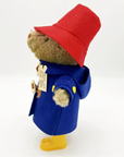 Side view of Paddington Bear soft toy in a blue toggle coat, red hat, and yellow boots.