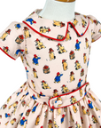 Pink cotton girls' dress with vintage print, red piped collar, and classic silhouette—an heirloom-quality outfit with timeless charm.