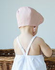Back view of a baby wearing a shell pink scalloped linen bonnet, showcasing the detailed edging.