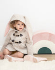 A young girl wearing the Little Goodall Snowshoe Rabbit Coat in merino wool, featuring a bunny ear hood, double-breasted front, and soft faux fur lining.