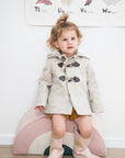 Toddler wearing Snowshoe Rabbit Coat made of Merino wool with toggle closures and faux fur lining.