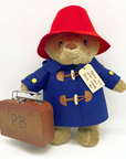 Classic 16-inch Paddington Bear plush in a red hat and blue wool coat, holding a suitcase with a tag that reads 'Please Look After This Bear