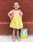 Smiling young girl wearing a lemon print dress with a pink backpack, ready for back to school