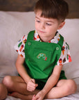 Toddler boy wearing the Very Hungry Caterpillar Party Food Shirt with green overalls, featuring an embroidered caterpillar on the front pocket.