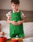 Toddler standing in a green Hungry Caterpillar romper with embroidered detail, layered over a food print shirt, with snack bowls on a wooden tray.