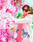 Young girl in a pink zebra-appliqué coat, accessorized with a bow and sunglasses, near blooming flower