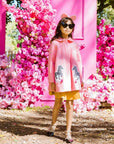 Girl wearing Yolanda and Tatty pink wool coat with zebra appliqués, styled with a skirt and bow, in a floral setting