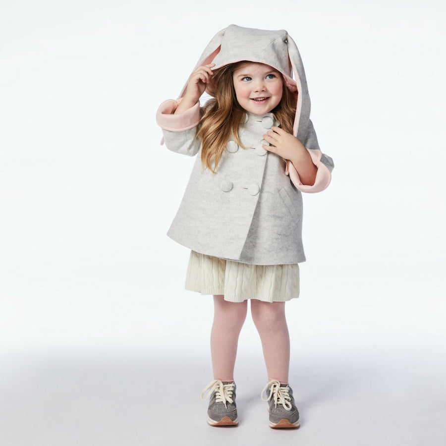 girl modeling grey bunny coat, holding up hood.