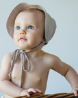 Baby wearing a flax linen wide-brim sun bonnet in wheat color with chin ties for sun protection.