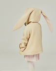 Back view of the tan bunny coat on the model, displaying floppy bunny ears with the hood up.