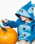 a boy wearing the Blithe Blue Dinosaur Coat , a cozy wool blend jacket with a hood, button closure, and playful dinosaur design