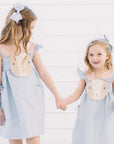 Two young girls wearing blue gingham bunny dresses by Little Goodall, each with matching blue gingham hair bows