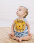 Baby in Blue Gingham Lion Romper sitting on a woven rug, gazing upward. Features lion face appliqué with ruffled mane. Childsware for boys and girls