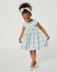 Girl in a mint Carrot and Dot Dress with a bamboo trellis print, cap sleeves, and a balloon skirt, looking down while holding the side of her dress