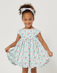 Girl in the Carrot and Dot Dress in mint & plum with a bamboo trellis print, cap sleeves, and a balloon skirt, holding the sides of her dress