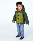 boy wearing the Little Goodall Cheeky Green Dinosaur Coat, a wool-felt jacket with big buttons, a soft plush lining, and a playful dino-inspired design