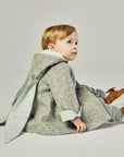 Seated child in a Little Goodall grey bunny coat, showcasing floppy ears with a light blue lining.