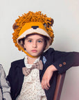 boy wearing a handmade wool-blend felt lion hat with a sherpa lining, earflaps, and a velcro chin strap, featuring a playful yarn mane.