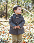 Toddler wearing the brown wool Flopsy Bunny Coat with toggle closures and a cozy hood, standing in a sunlit autumn forest