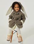 girl sitting on a stool wearing the Little Goodall Flopsy Bunny Coat, a cozy wool jacket with floppy bunny ears and toggle closures, perfect for winter