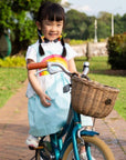 Smiling girl riding a bike in a sky blue sundress with a rainbow applique and cloud peplum
