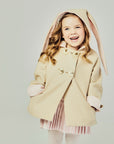 Tan bunny coat on model with her sleeve cuffs rolled up and hands in the coat pockets.