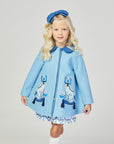 Girl wearing the Aldrich and Madame De Bleu coat, a light blue wool coat with embroidered Staffordshire dogs, tasseled details, and a Peter Pan collar