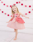Girl smiling and twirling in Little Goodall pink flamingo dress with layered peplum and flamingo applique