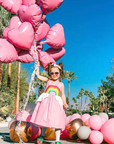Little Girls pink sundress with appliqued rainbow on the front, full skirt, and white peplum shaped like clouds.
