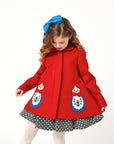 Close up of girl modeling red coat while wearing a polkadot dress underneath and a blue bow on top of her head.
