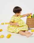 Toddler in a Very Hungry Caterpillar™ Lemonade Dress plays with fresh lemons