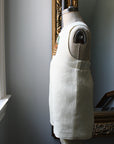 Side view of ivory linen bunny romper on a dress form, showcasing fabric texture and embroidered detail."