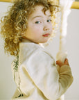 Child wearing an ivory cotton Paddington Bear sweater featuring classic Peggy Fortnum illustrations, soft knit fabric, ribbed cuffs, and shoulder buttons