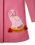 Close-up of embroidered dog motif on pink wool coat, featuring a tufted pillow with tassel details